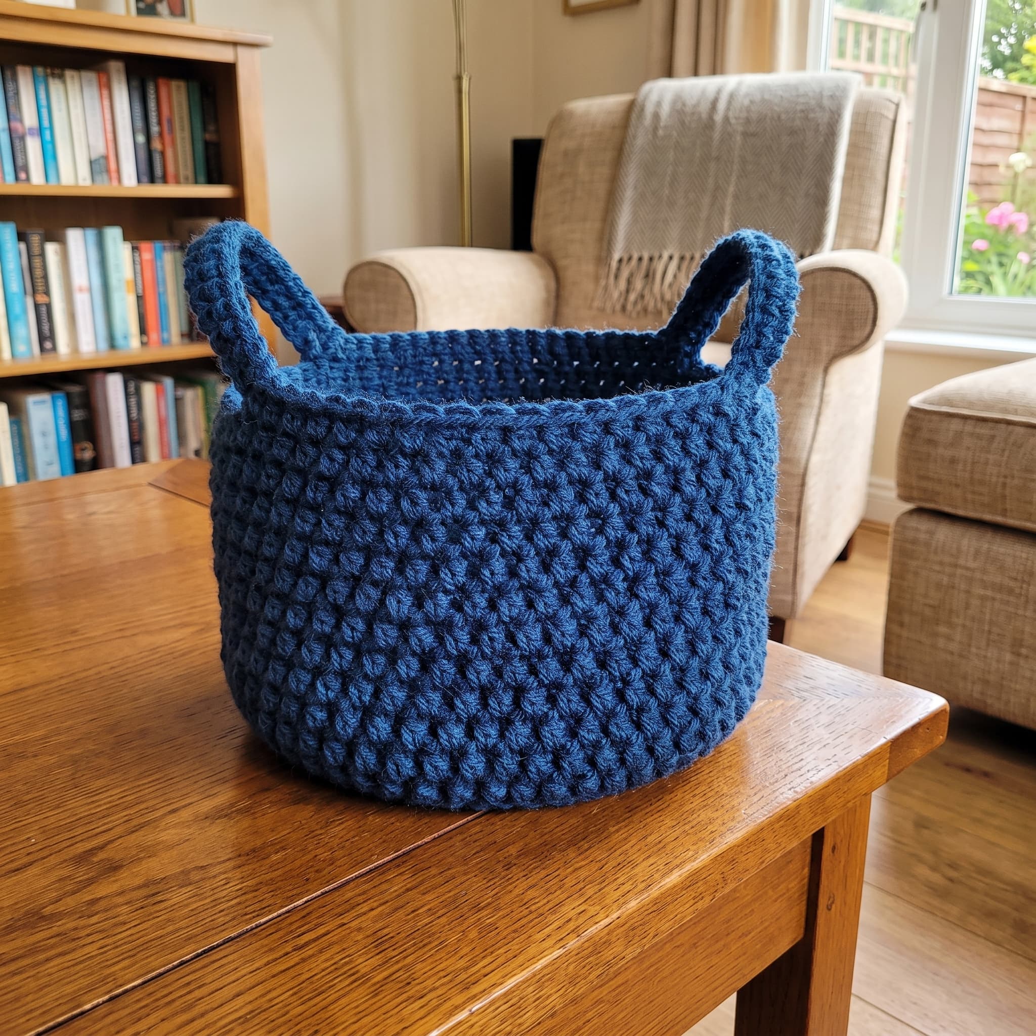 Navy blue crochet storage basket with handles on a wooden table by a bookshelf