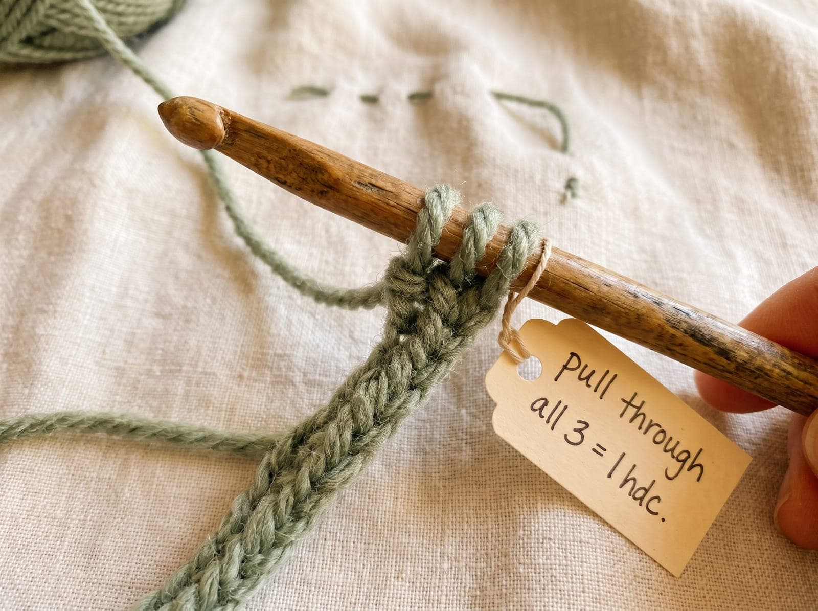 Pulling yarn through all three loops to complete one half double crochet.
